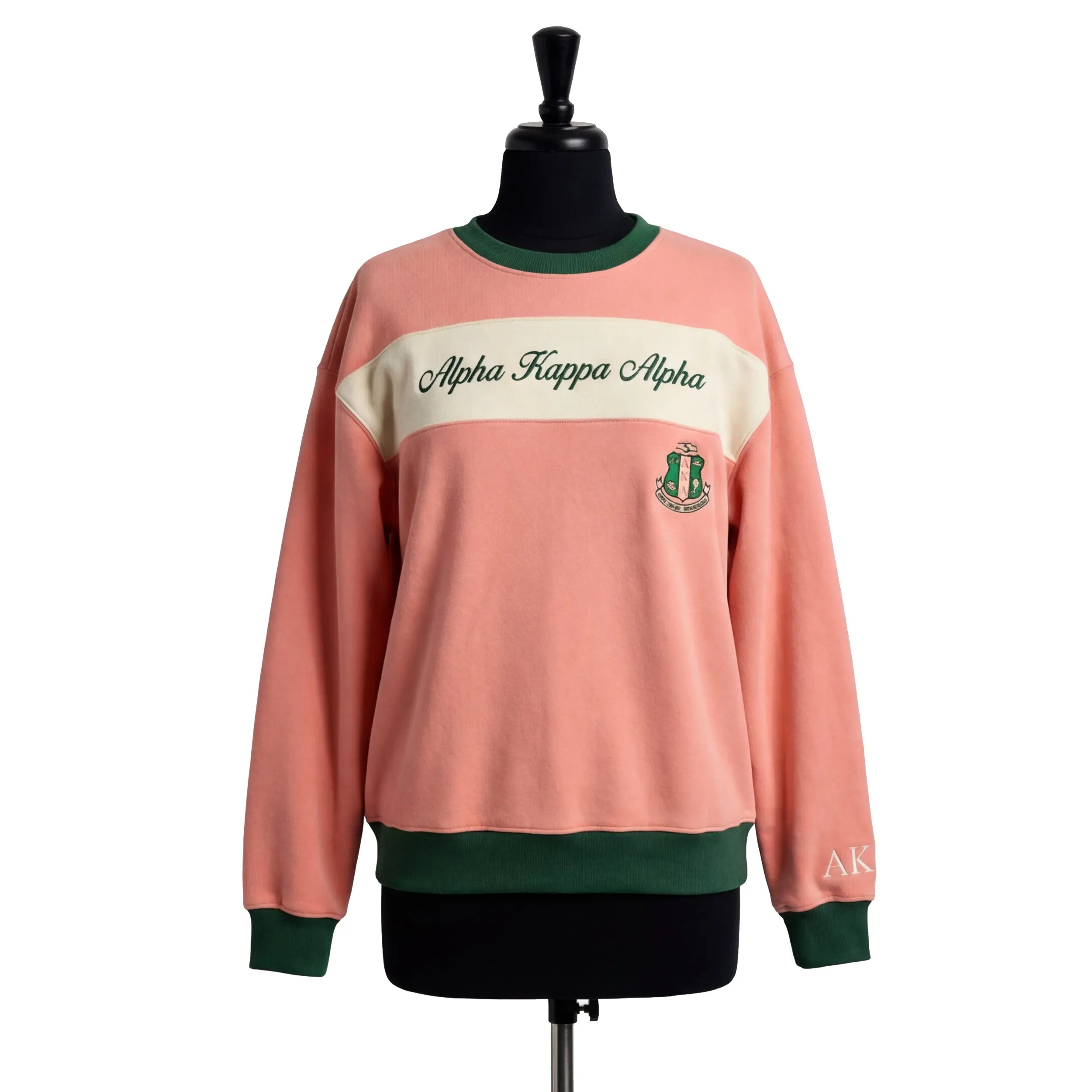 Pink sweatshirt with green accents and 'Alpha Kappa Alpha' text on a mannequin against a white background