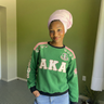 Woman wearing AKA Alpha Kappa Alpha green crewneck sorority sweatshirt with 1908 sleeve and rose embroidery styled with jeans
