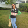 Woman wearing AKA Alpha Kappa Alpha black green rugby polo shirt with pink AKA stripe and ivy shoulder embroidery styled with jeans
