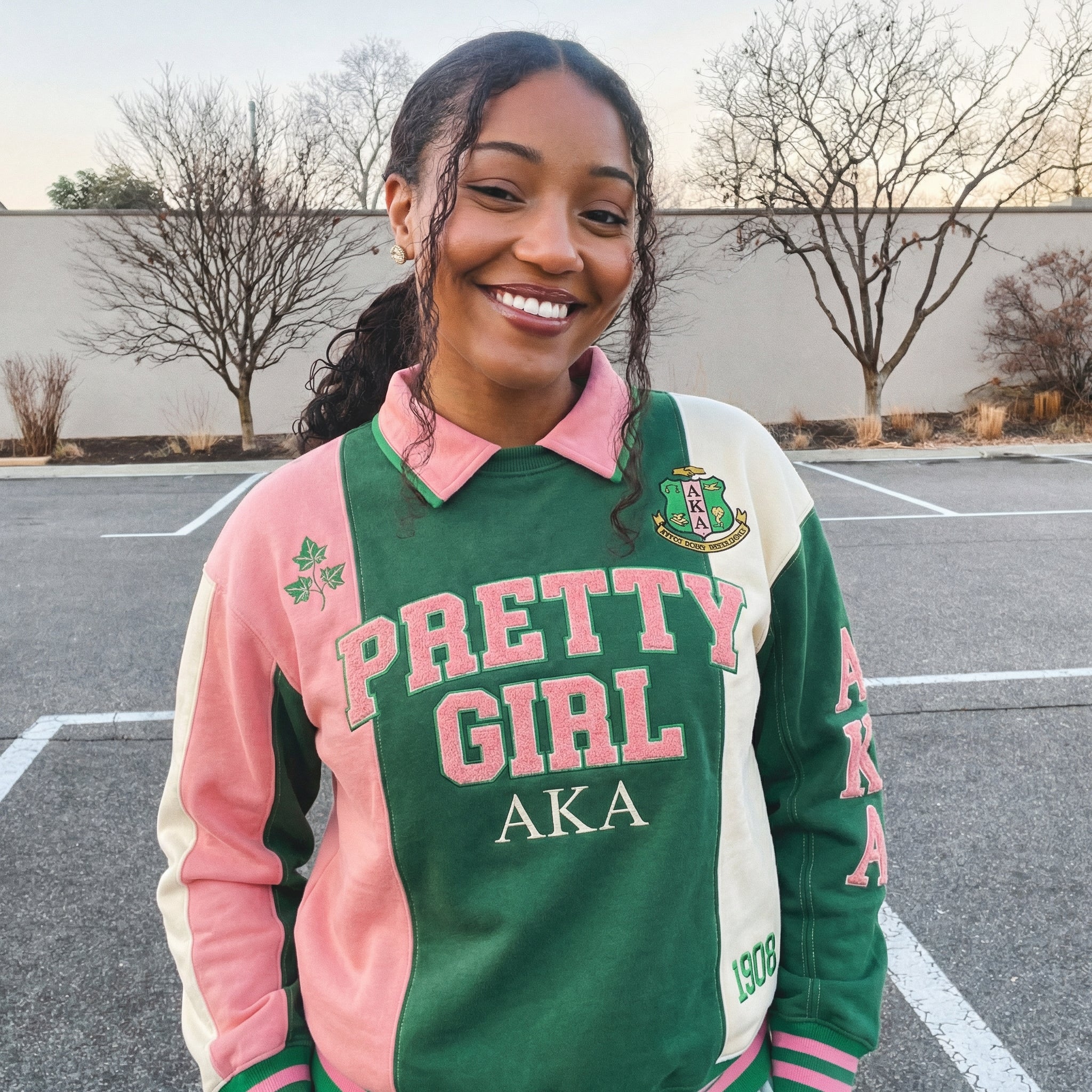 Person wearing a green, pink, and white jacket with 'Pretty Girl AKA' text in a parking lot.