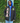 Person wearing a black jacket with 'AKA' letters and a crest, standing against a green leafy background.