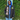 Person wearing a black jacket with 'AKA' letters and a crest, standing against a green leafy background.