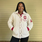 Person wearing a cream-colored fleece jacket with a logo and text, standing against a beige wall.